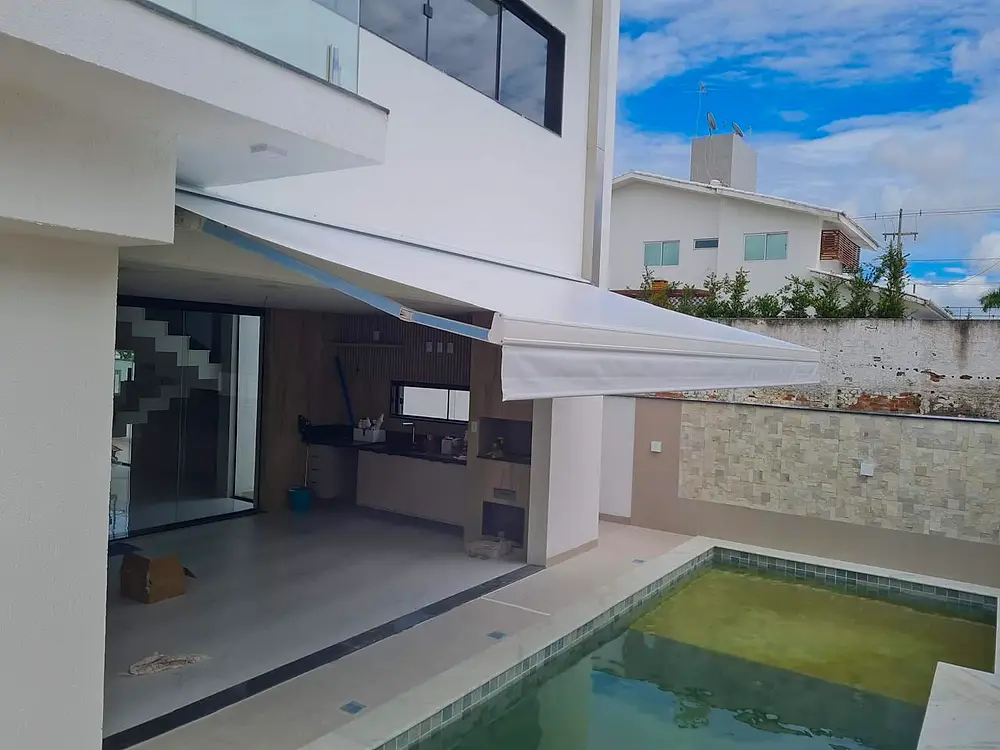 Área externa com piscina e toldo retrátil sobre a estrutura.