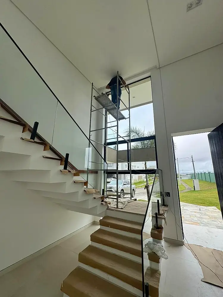 Instalador trabalhando em uma janela alta ao lado de uma escada, com apoio de andaime.